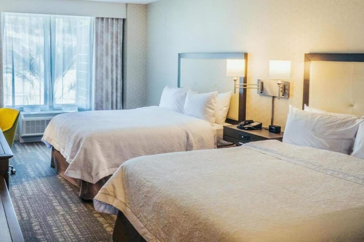 Una camera d'albergo con due letti, una scrivania, una sedia e un'ampia finestra con tende.