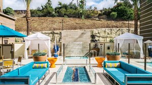 A pool area with blue lounge chairs, a water feature, and a view of a landscaped hillside. - Hampton Inn & Suites Mission Viejo (Mission Viejo)