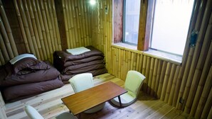 A compact room with a wooden floor, a small table, two chairs, and a sofa with cushions. - WORLDTRECK DINER & GUESTHOUSE - Pise - Hostel (Nagano)
