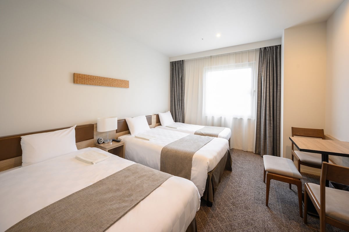 A hotel room with three beds, a desk, and a chair.