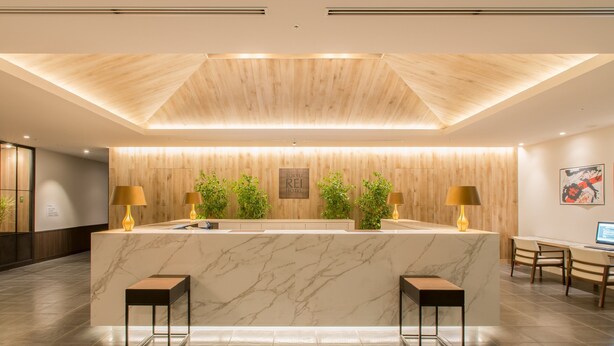 Een moderne receptiebalie met een marmeren blad, een wand van houtpanelen en twee bijzettafels.