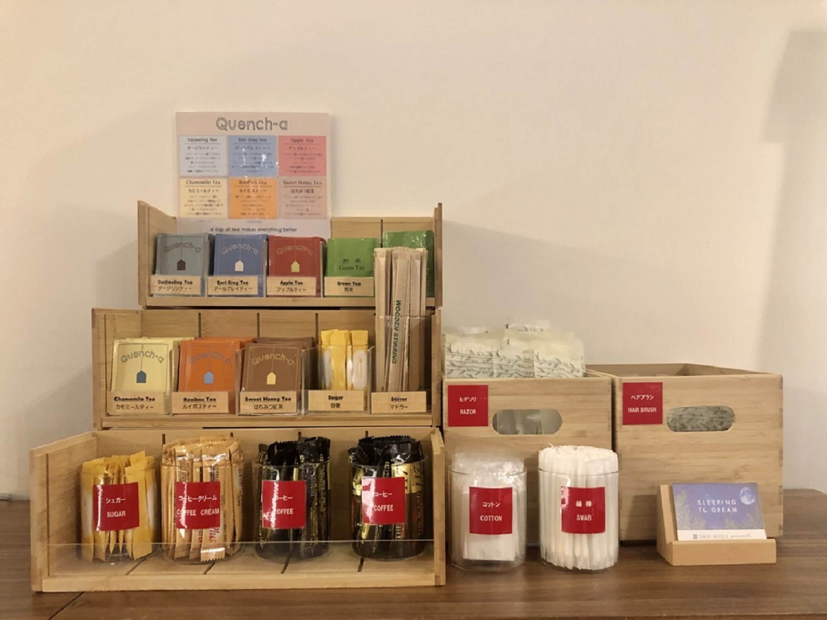 Une exposition de divers produits liés au thé et au café, notamment des sachets de sucre, de la crème pour le café et du café en grains, ainsi que des pailles en bois et un livre intitulé « Dormir pour rêver ».