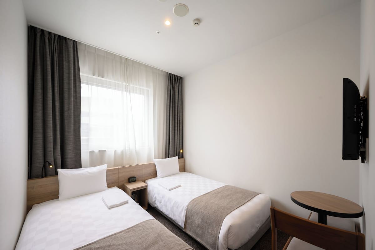 A hotel room with two beds, a small table, and a TV mounted on the wall.