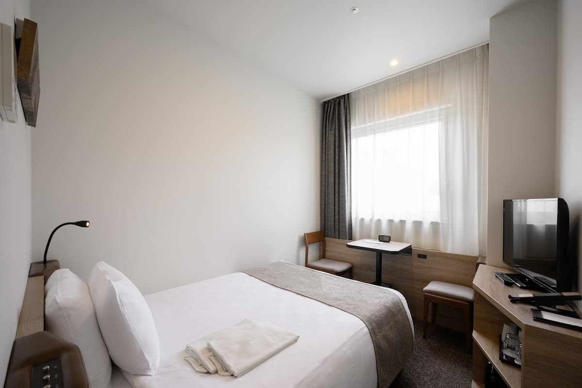 A hotel room with a large bed, a desk, a chair, a television, and a window with curtains.