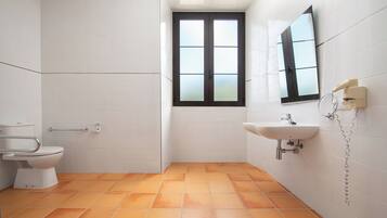 Un baño con azulejos blancos, inodoro, lavamanos y ventana.