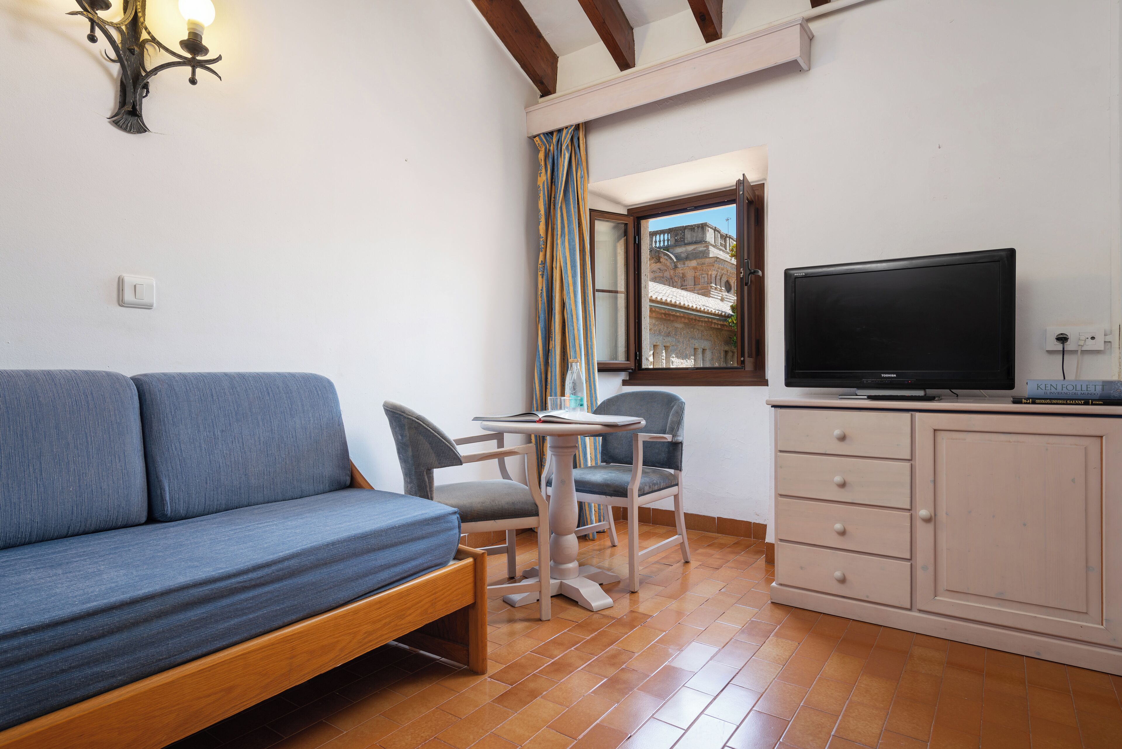 A room with a sofa, a chair, a small table, a TV, and a window with a view of buildings.