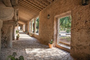 A corridor with stone walls, wooden beams, and potted plants. - Santuari de Lluc (Escorca)