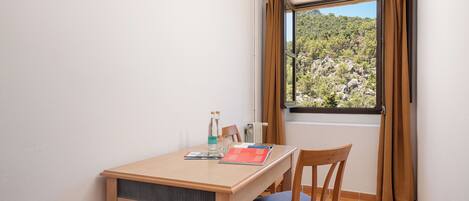 Una habitación pequeña con una mesa de madera, una silla y una ventana con cortinas.