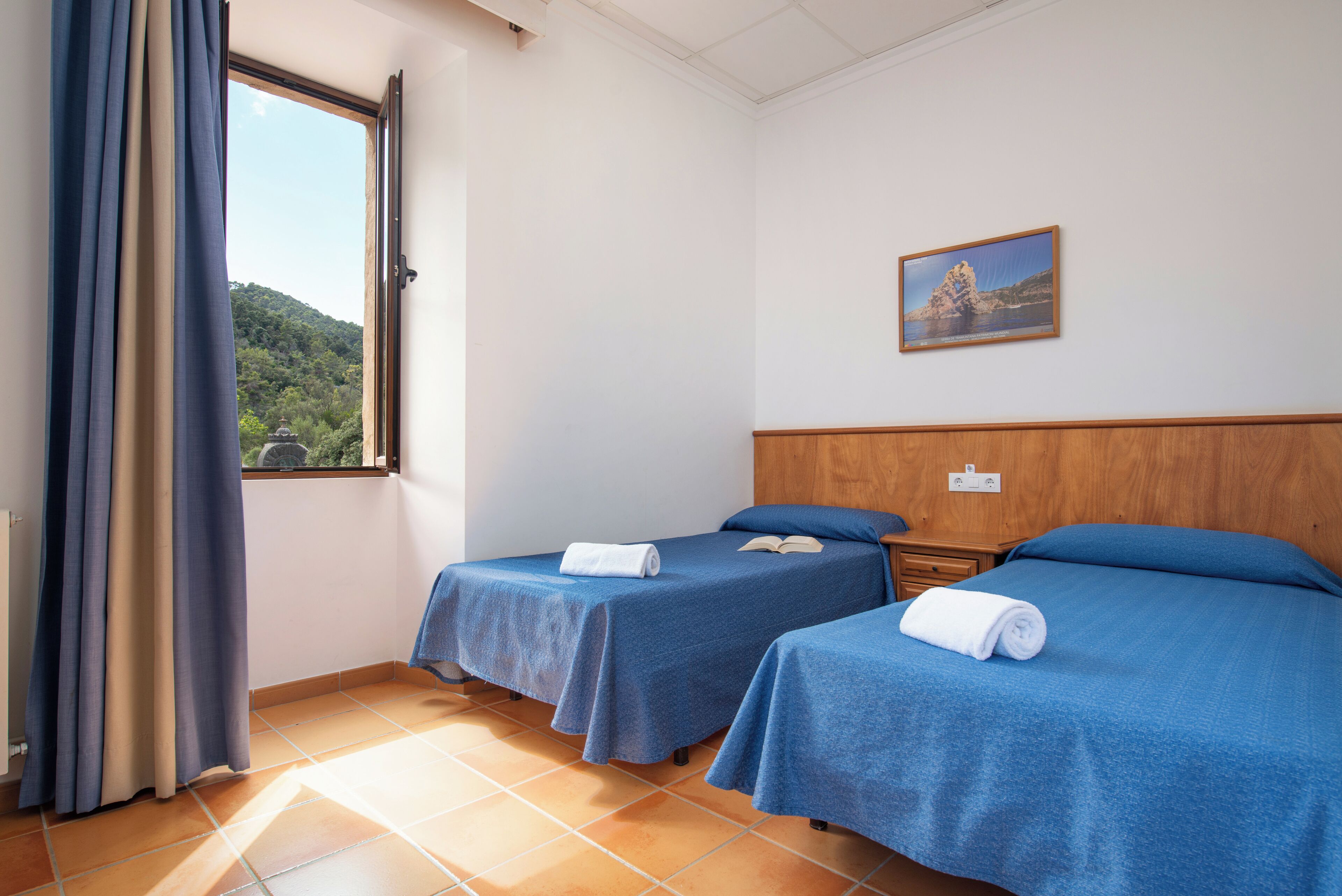 A hotel room with two beds, a window with curtains, a painting on the wall, and a tiled floor.