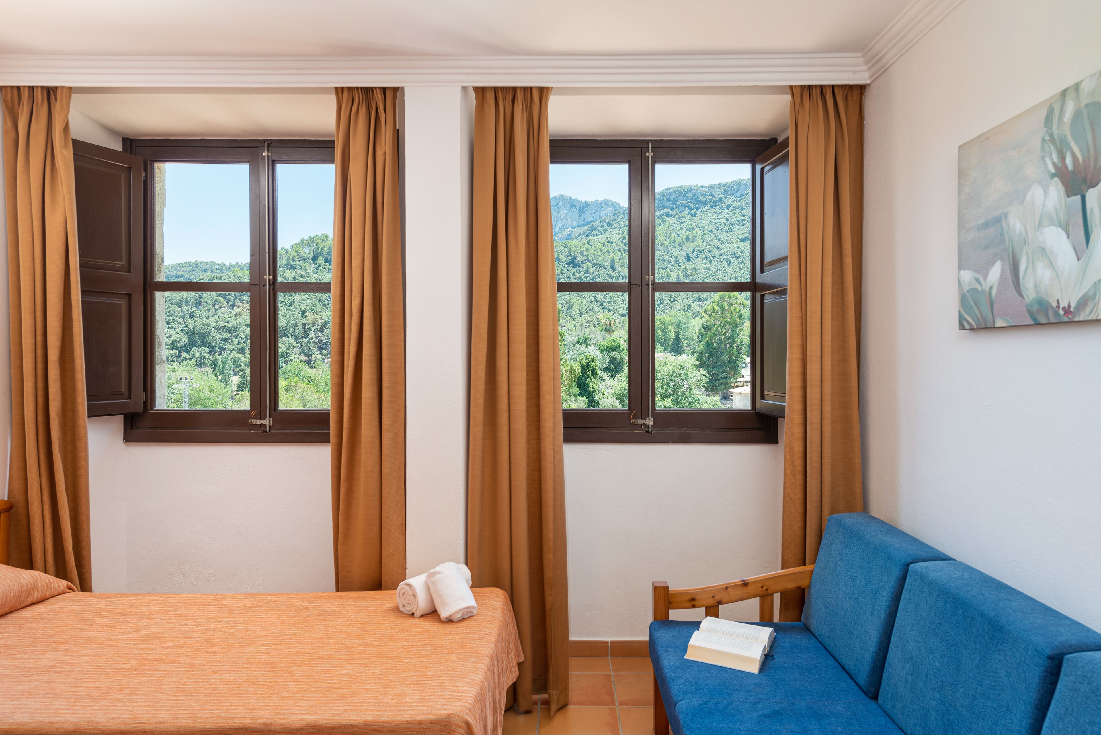 Une chambre d’hôtel avec un lit, un canapé bleu et une fenêtre avec des rideaux.