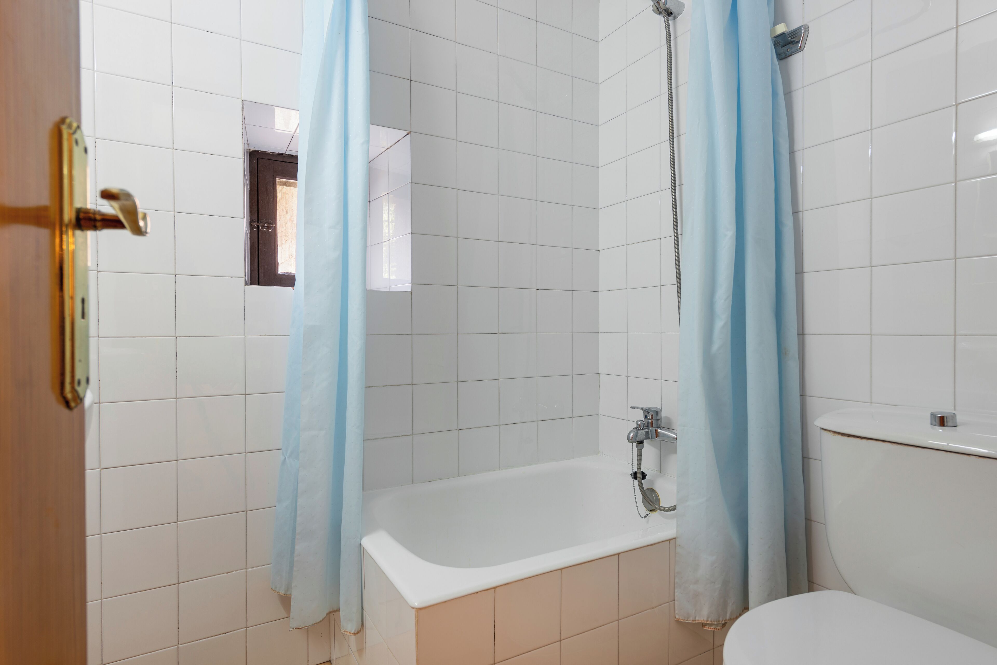 Une salle de bain avec des murs recouverts de carreaux blancs, une baignoire et un rideau de douche.