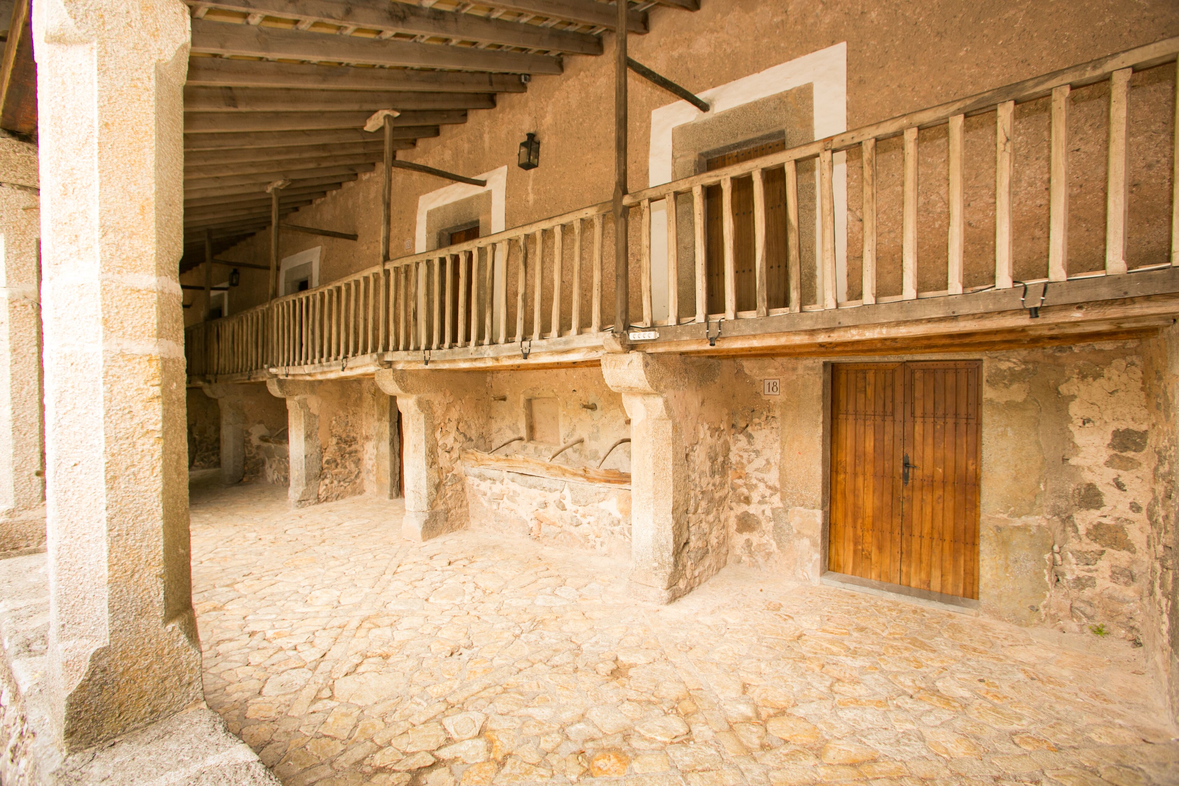 A stone courtyard with a wooden door and a balcony with a railing.