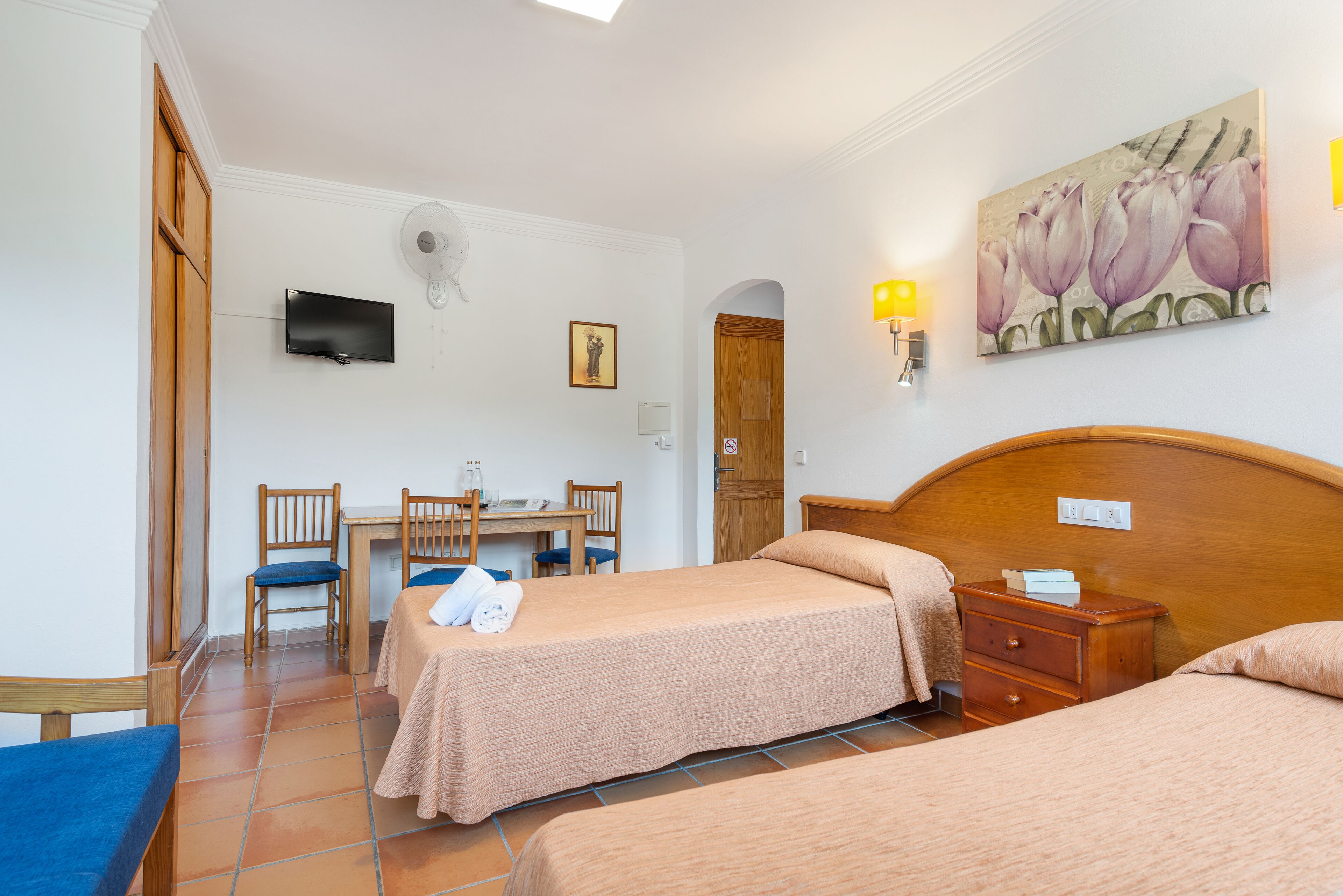 Una camera d'albergo con due letti, una scrivania con sedie, una televisione e un quadro appeso al muro.