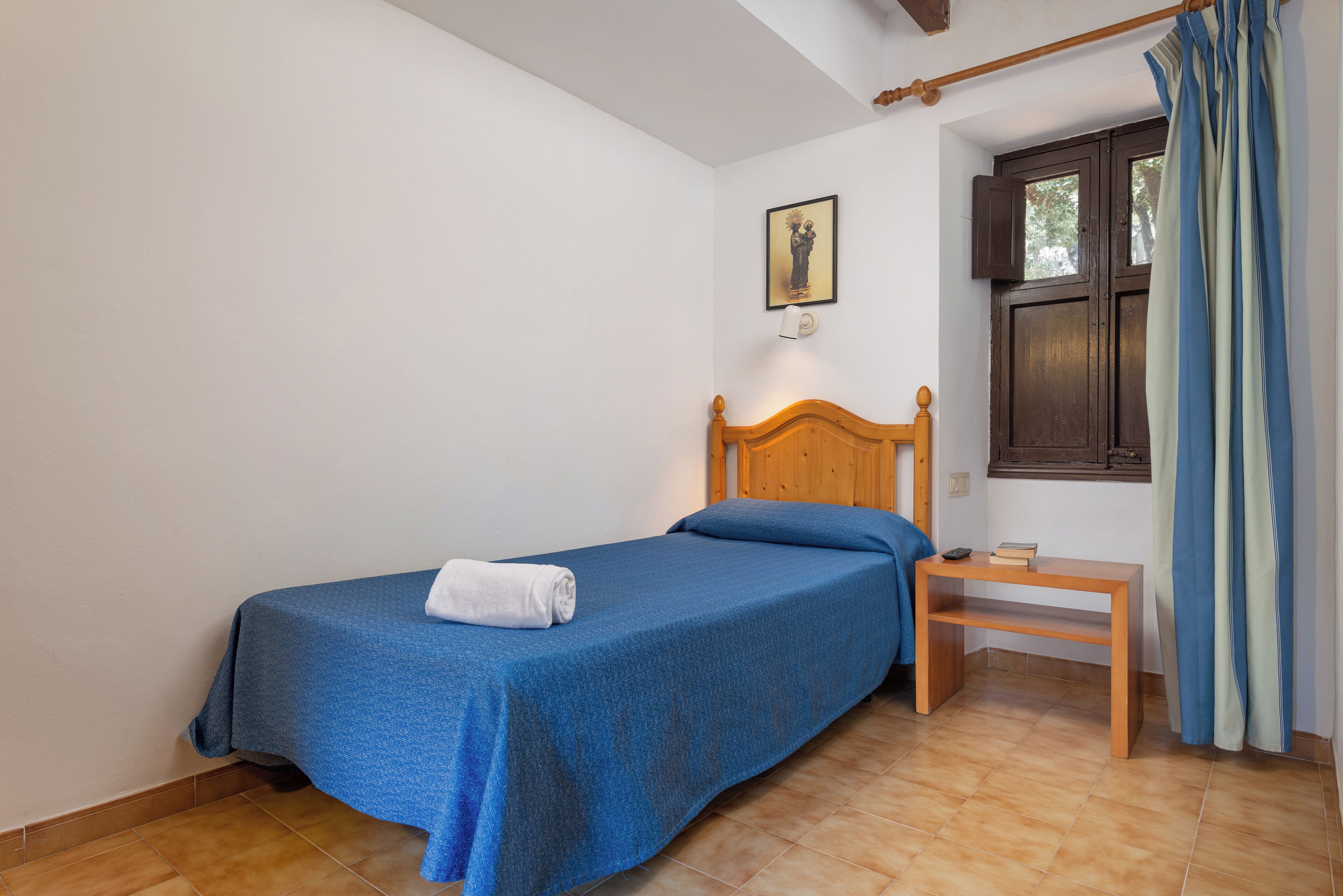 Un letto singolo con una testiera in legno, un comodino e una finestra con tende.