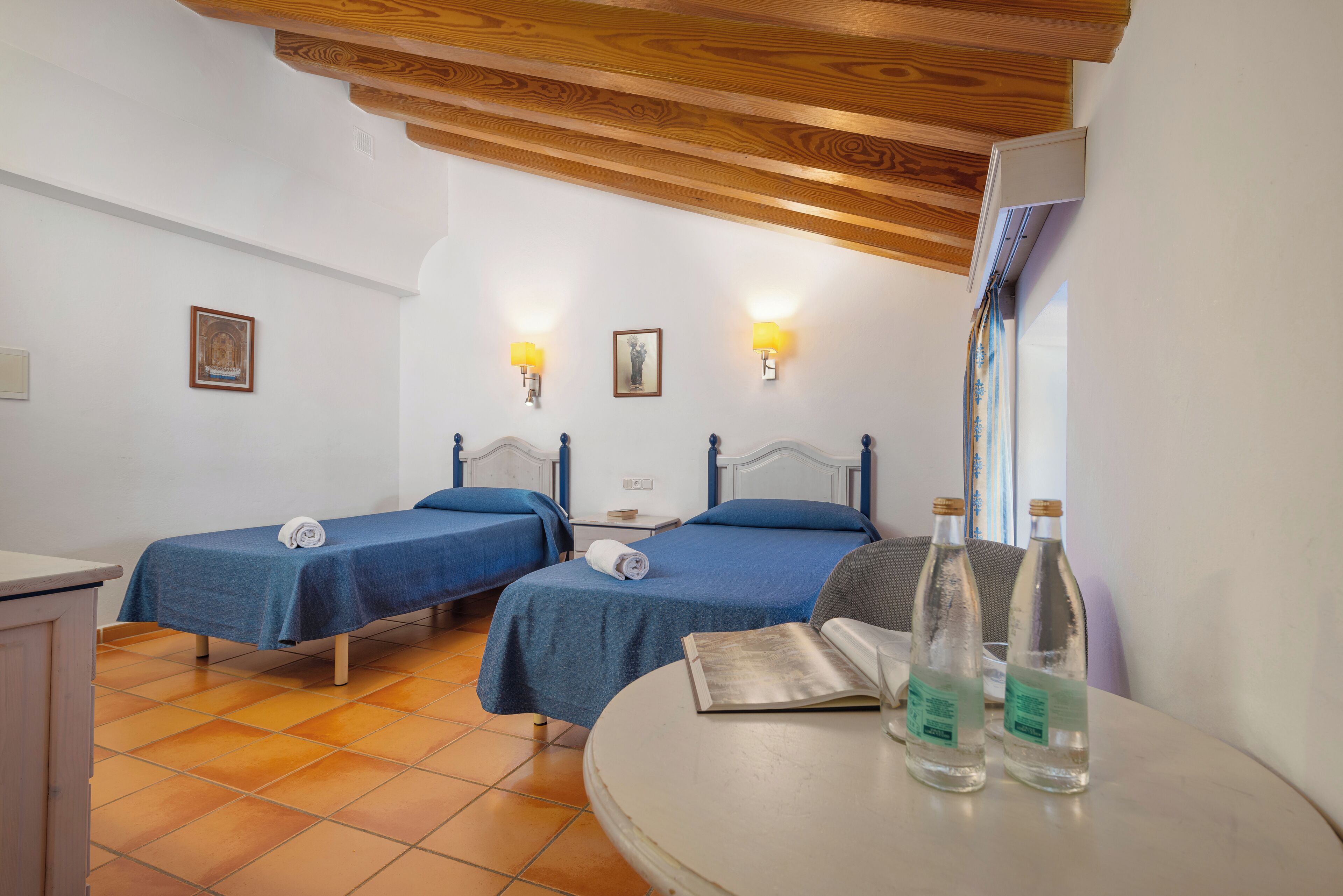 Une chambre d’hôtel avec deux lits, une petite table et une fenêtre avec des rideaux.