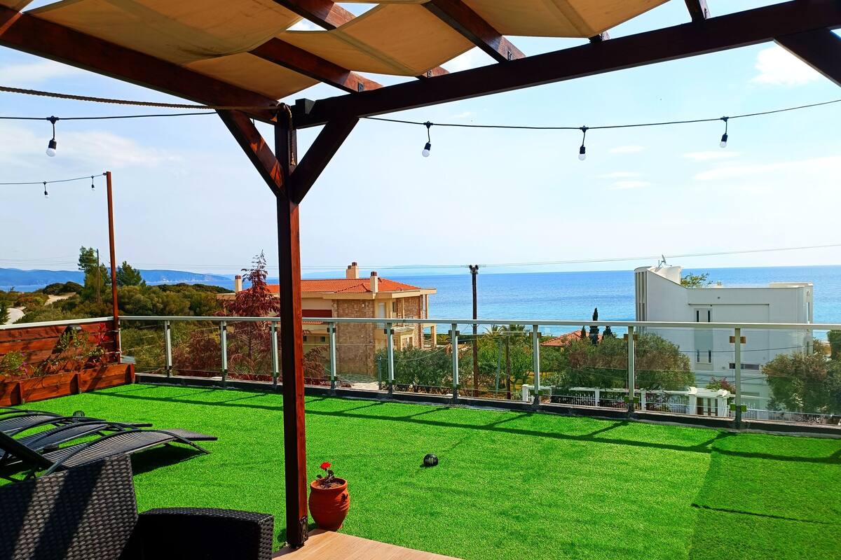 Une terrasse avec un revêtement de gazon synthétique, du mobilier d’extérieur et une vue sur la mer.
