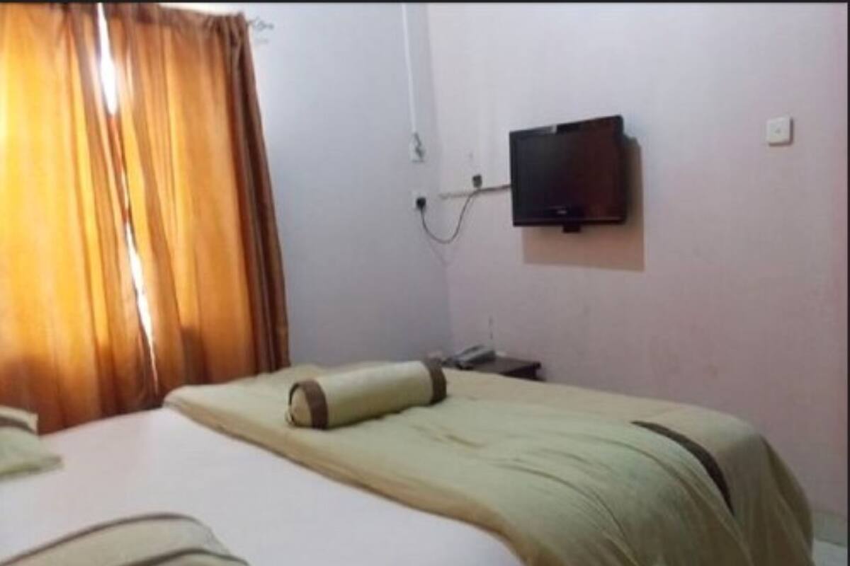 Ein Hotelzimmer mit Bett, Wandfernseher und einem fenster mit Vorhängen.