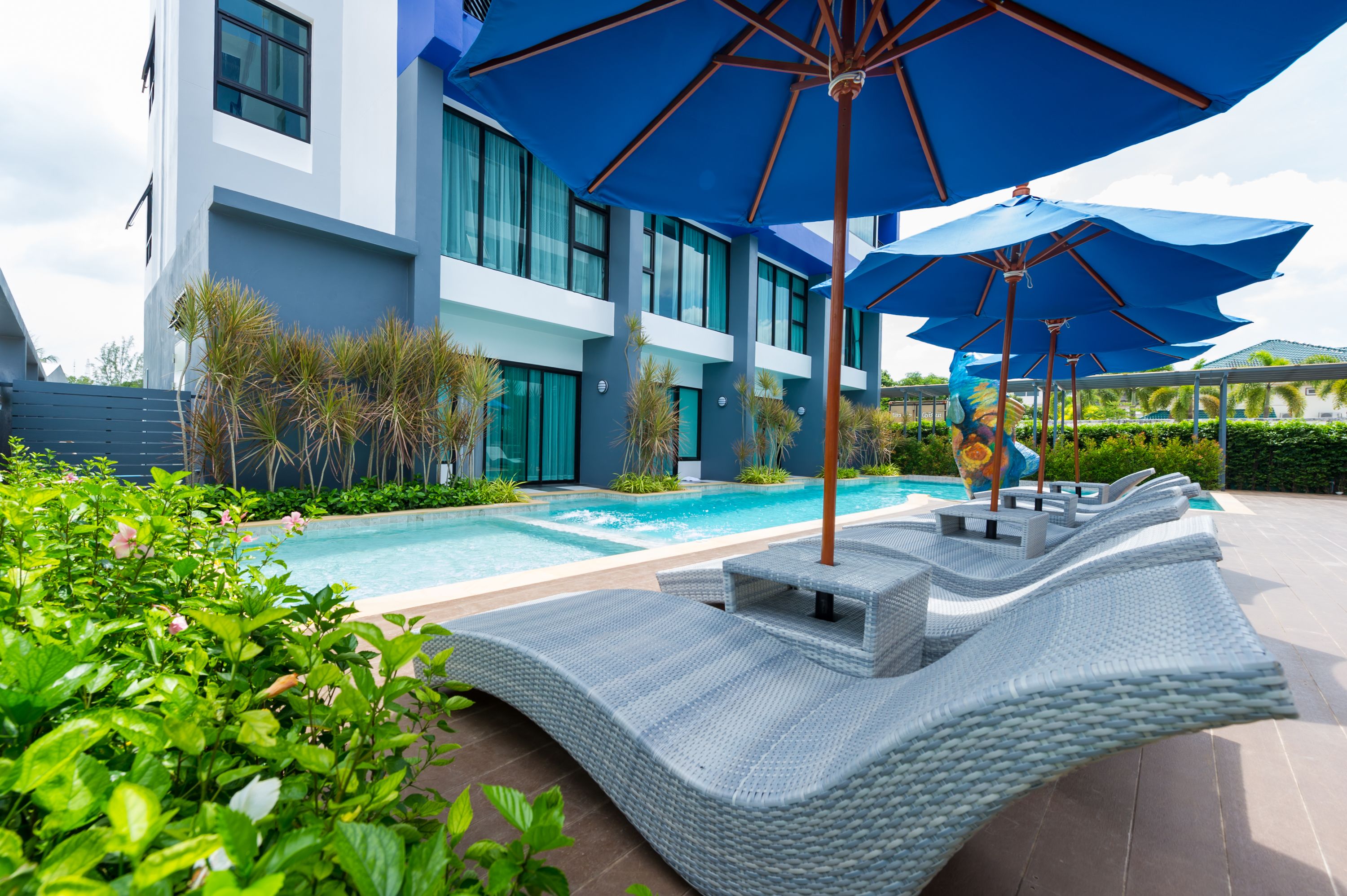 Un hotel moderno con piscina, sombrillas azules y sillas de descanso.