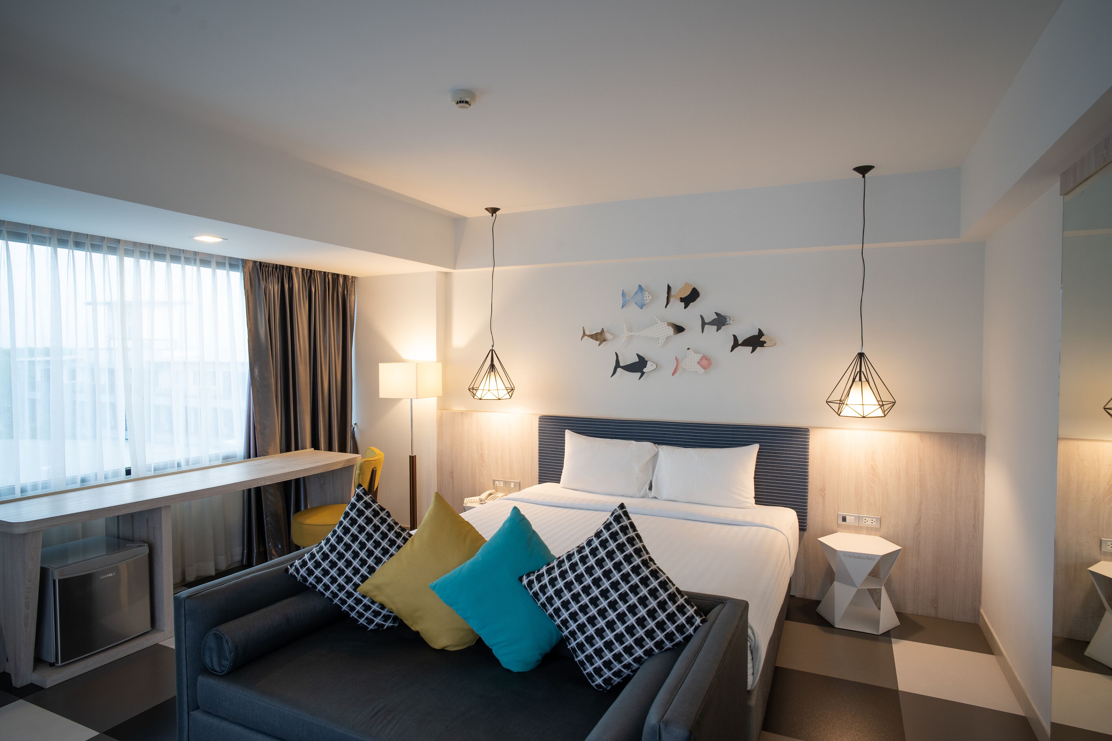 A modern hotel room with a bed, a sofa, a desk, and a wall-mounted fish decoration.