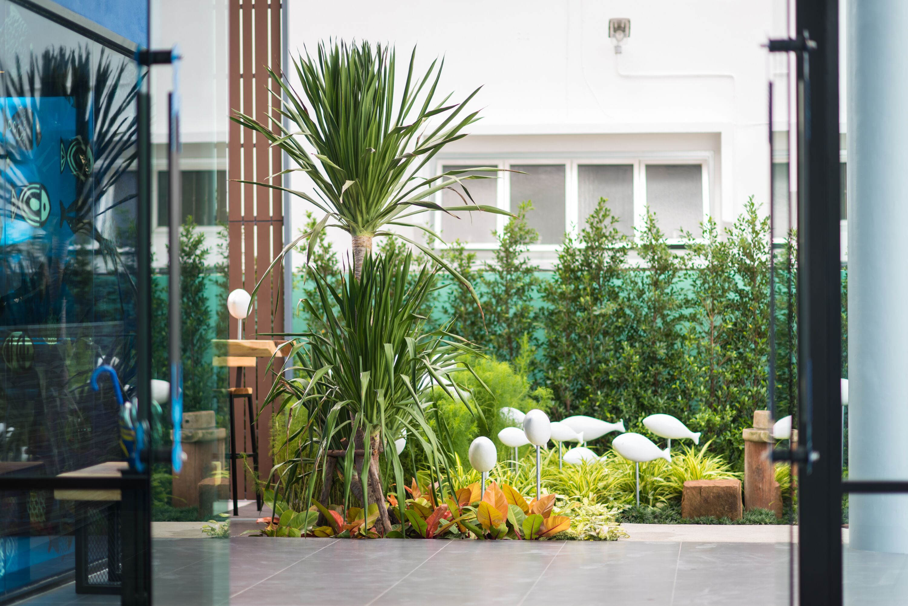 Un espacio exterior moderno con una palmera, diversas plantas y esculturas decorativas de aves.