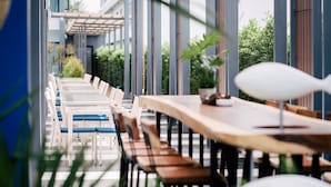 Un restaurante con mesas y sillas largas, suelo de madera y plantas en macetas.