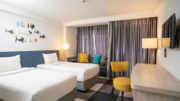 A hotel room with two beds, a sofa, a chair, a flat-screen TV, and a wall-mounted lamp.