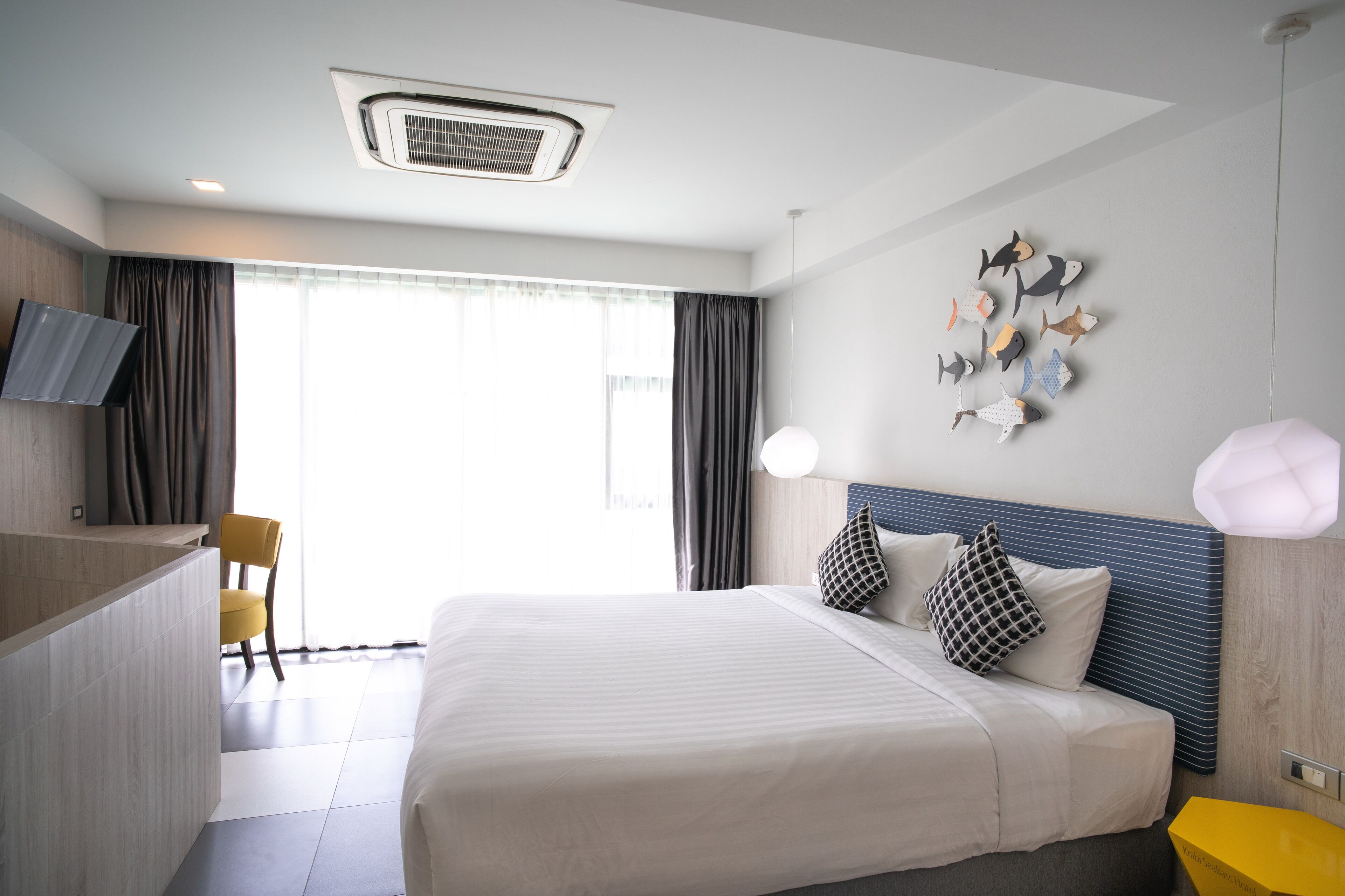 A modern hotel room with a large bed, a flat-screen TV, a desk, and a decorative fish wall art piece.