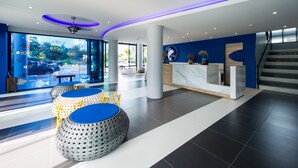 Un moderno vestíbulo de hotel con mostrador de recepción, zona de estar y grandes ventanales con vistas a un estacionamiento.
