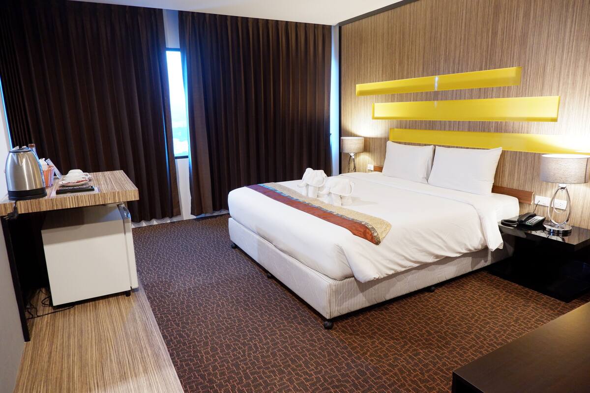 A hotel room with a large bed, a desk with a kettle, and a view of the outdoors through the window.