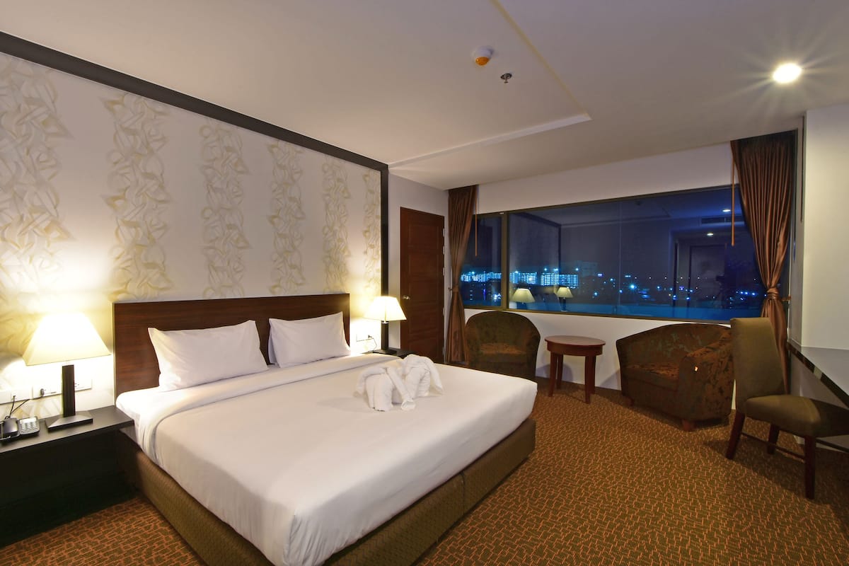 A hotel room with a large bed, two bedside tables with lamps, a chair, a small table, and a view of the city at night.