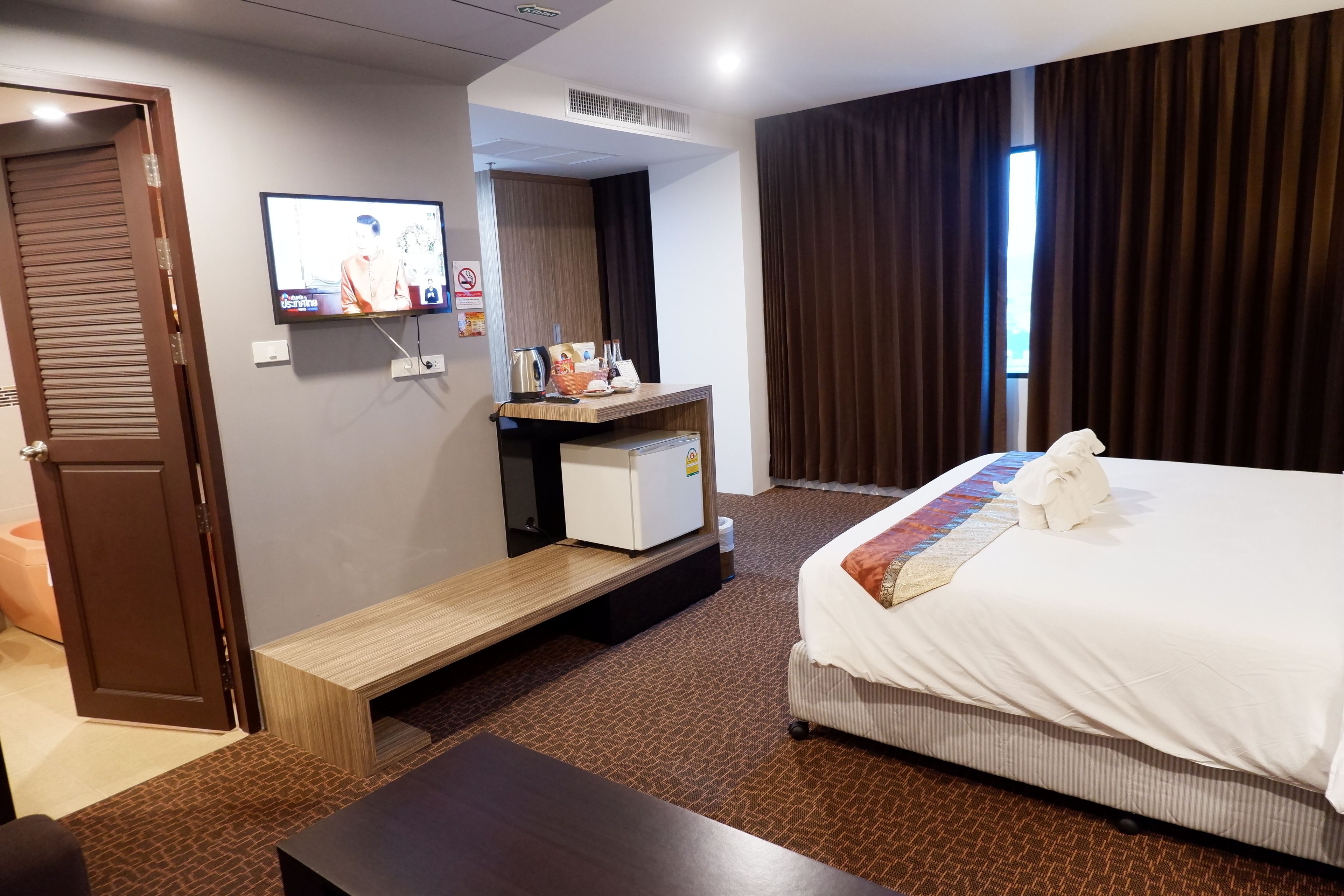 Ein Hotelzimmer mit einem Bett, einem Schreibtisch mit Computer, einem Fernseher und einem Fenster mit Vorhängen.