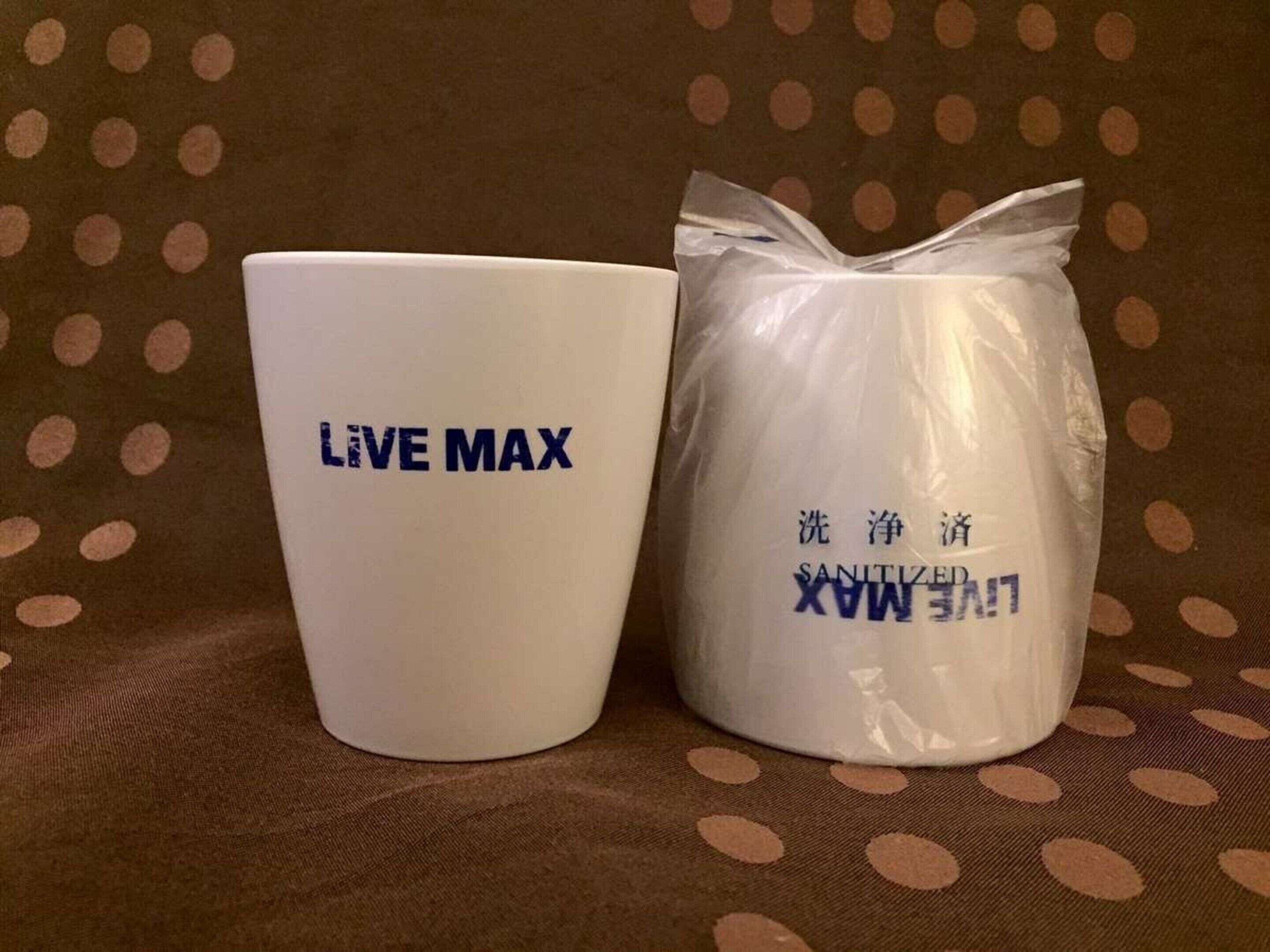 En hvid kop med teksten "LIVE MAX" og en hvid beholder med teksten "SANITIZER MAX" samt fremmedsprogstekst.