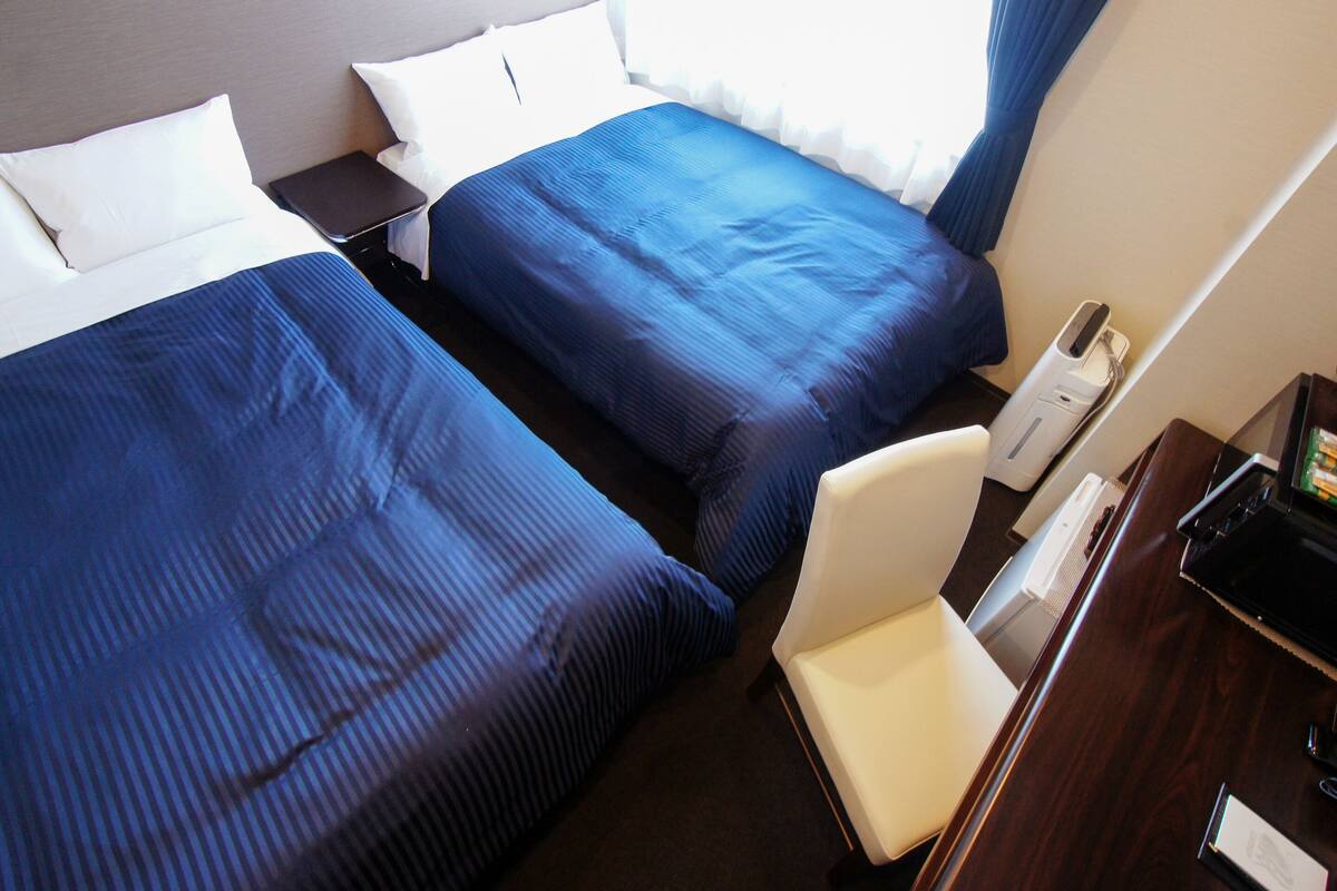 Une chambre d’hôtel avec deux lits, un bureau et une chaise.