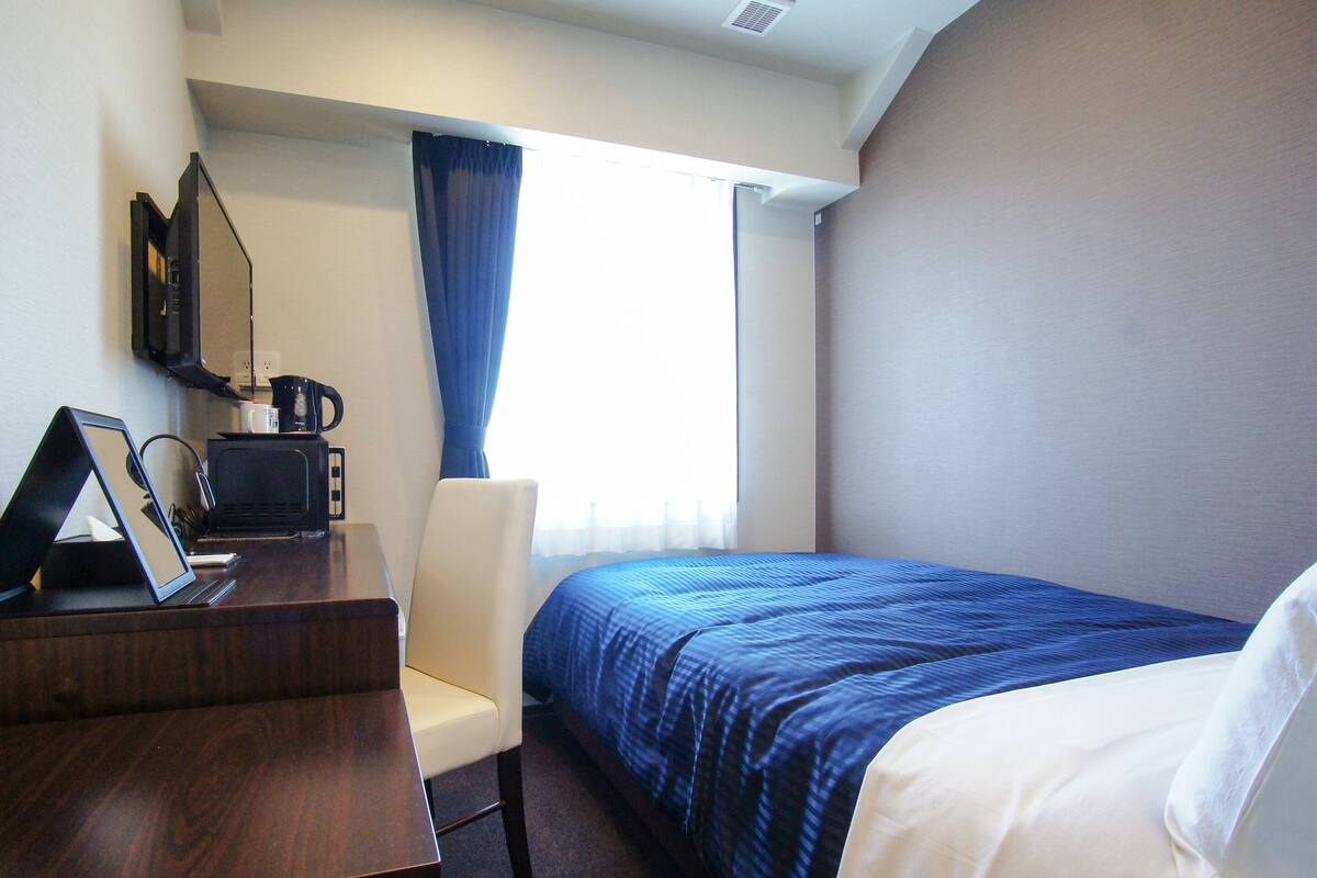 Une chambre d’hôtel comprenant un lit, un bureau avec un ordinateur portable, une chaise, une fenêtre avec des rideaux et un four à micro-ondes.