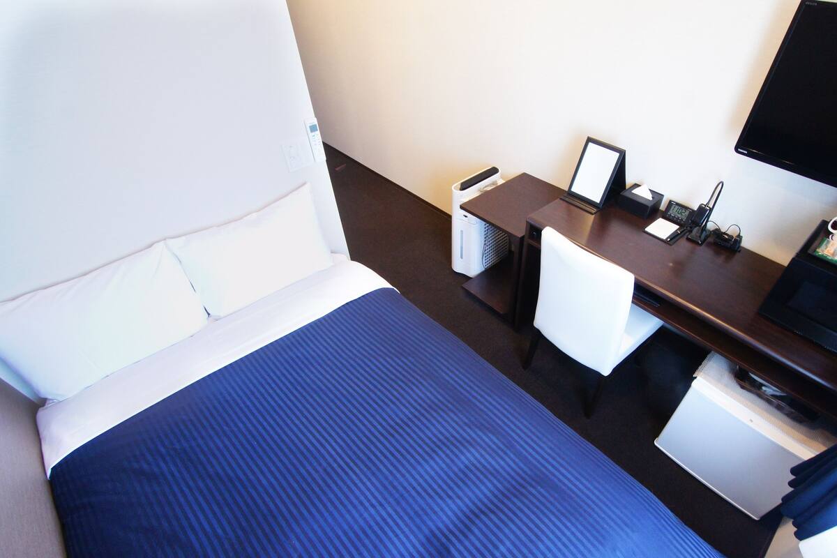 Une chambre d’hôtel avec un lit, un bureau, une chaise, une télévision et une petite table.