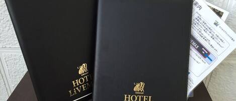 Twee zwarte ringbanden met de branding en het logo van 'HOTEL LIVEMAX', geplaatst op een tafel met wat papieren.