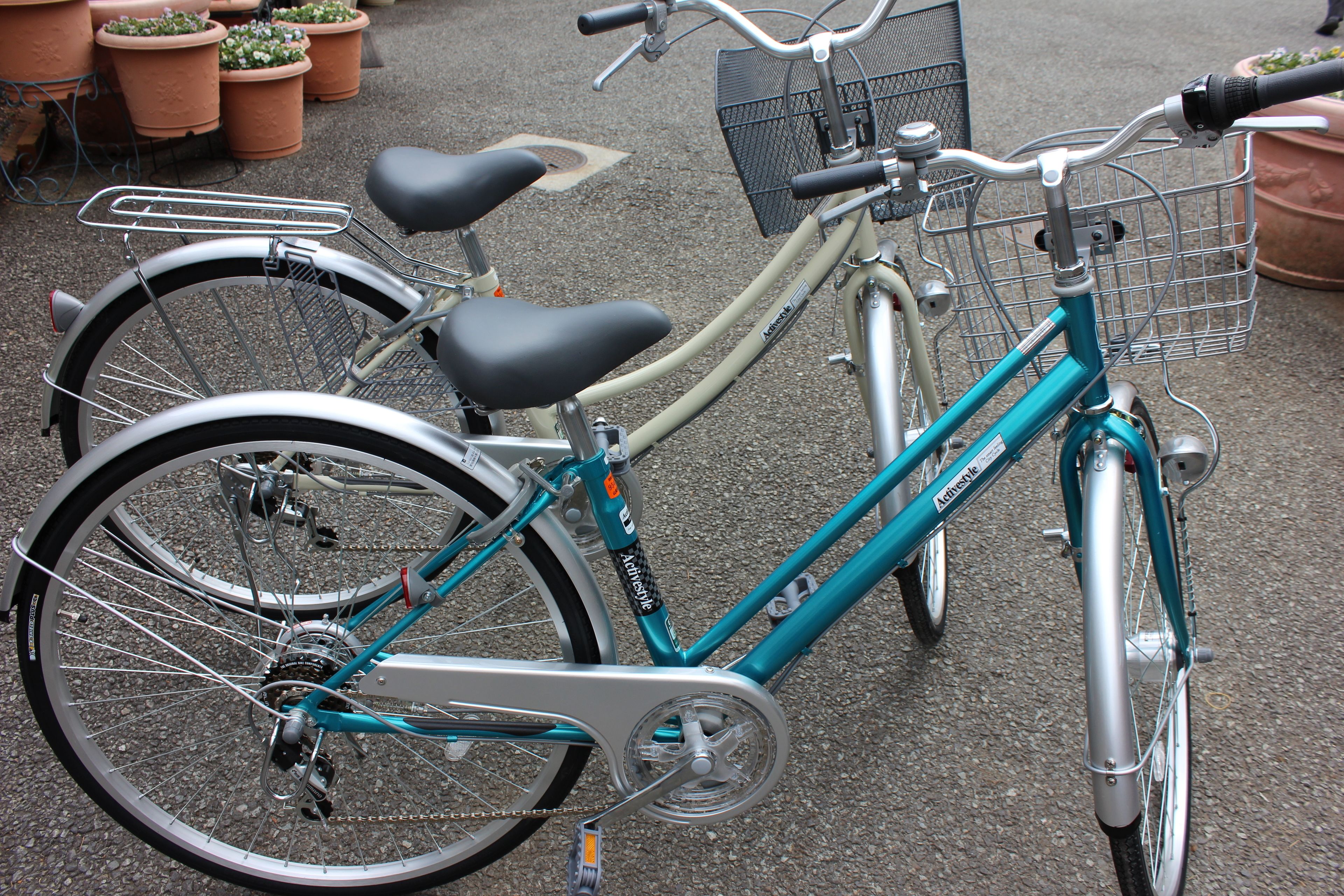 A teal bicycle with a basket and a seat, parked on a paved surface.