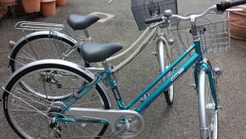 A teal bicycle with a basket and a seat, parked on a paved surface.