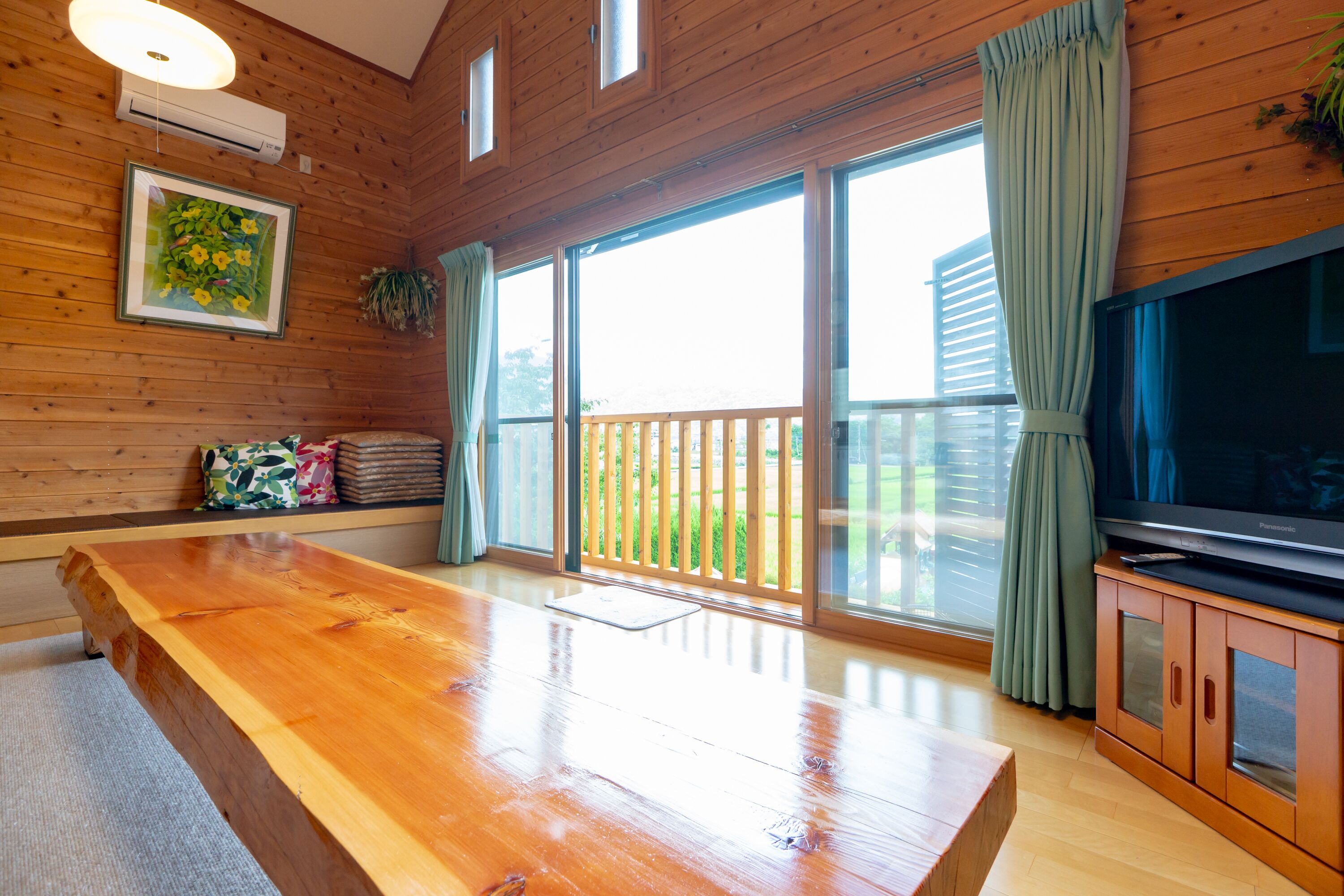 A wooden-paneled room with a large wooden table, a television on a wooden cabinet, and a sliding glass door leading to an outdoor area.