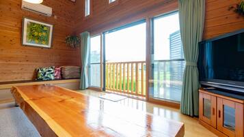 A wooden-paneled room with a large wooden table, a television on a wooden cabinet, and a sliding glass door leading to an outdoor area.