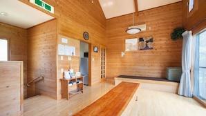 Een houten interieur met een lange tafel, een bank, een klok en een raam met gordijnen.