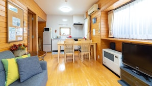 Een knus vertrek met houten inrichting, een eettafel met stoelen, een bank met kussens, een flatscreen televisie en een airconditioning.