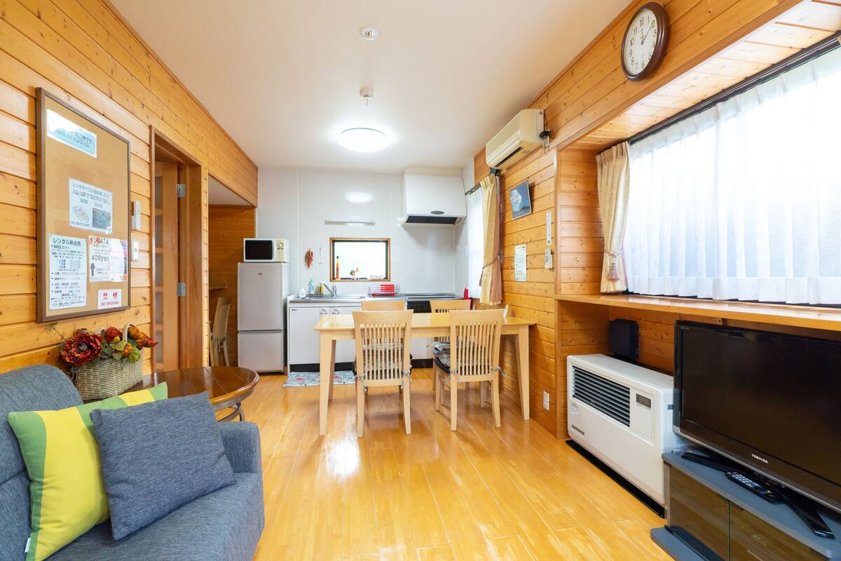 Een knus vertrek met houten inrichting, een eettafel met stoelen, een bank met kussens, een flatscreen televisie en een airconditioning.