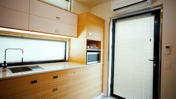 Een compacte keuken met een spoelbak, kastjes en een raam met zonwering.