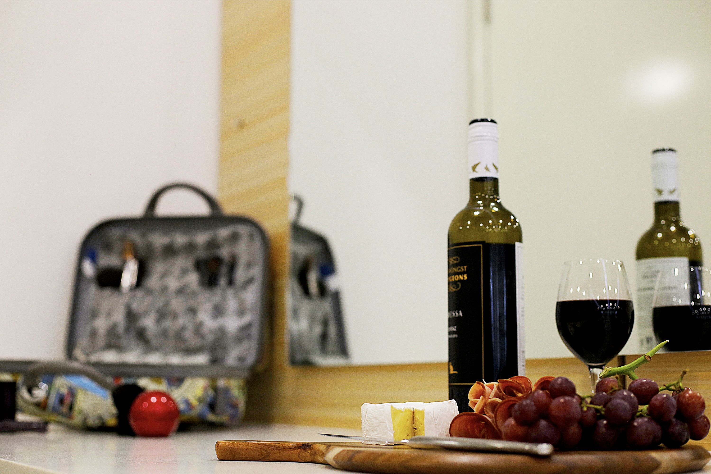 A table with a bottle of wine, two glasses of wine, a piece of cheese, a red apple, and a bunch of grapes.