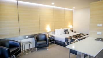 A modern hotel room with a bed, bedside tables, a desk, a chair, and a carpeted floor.