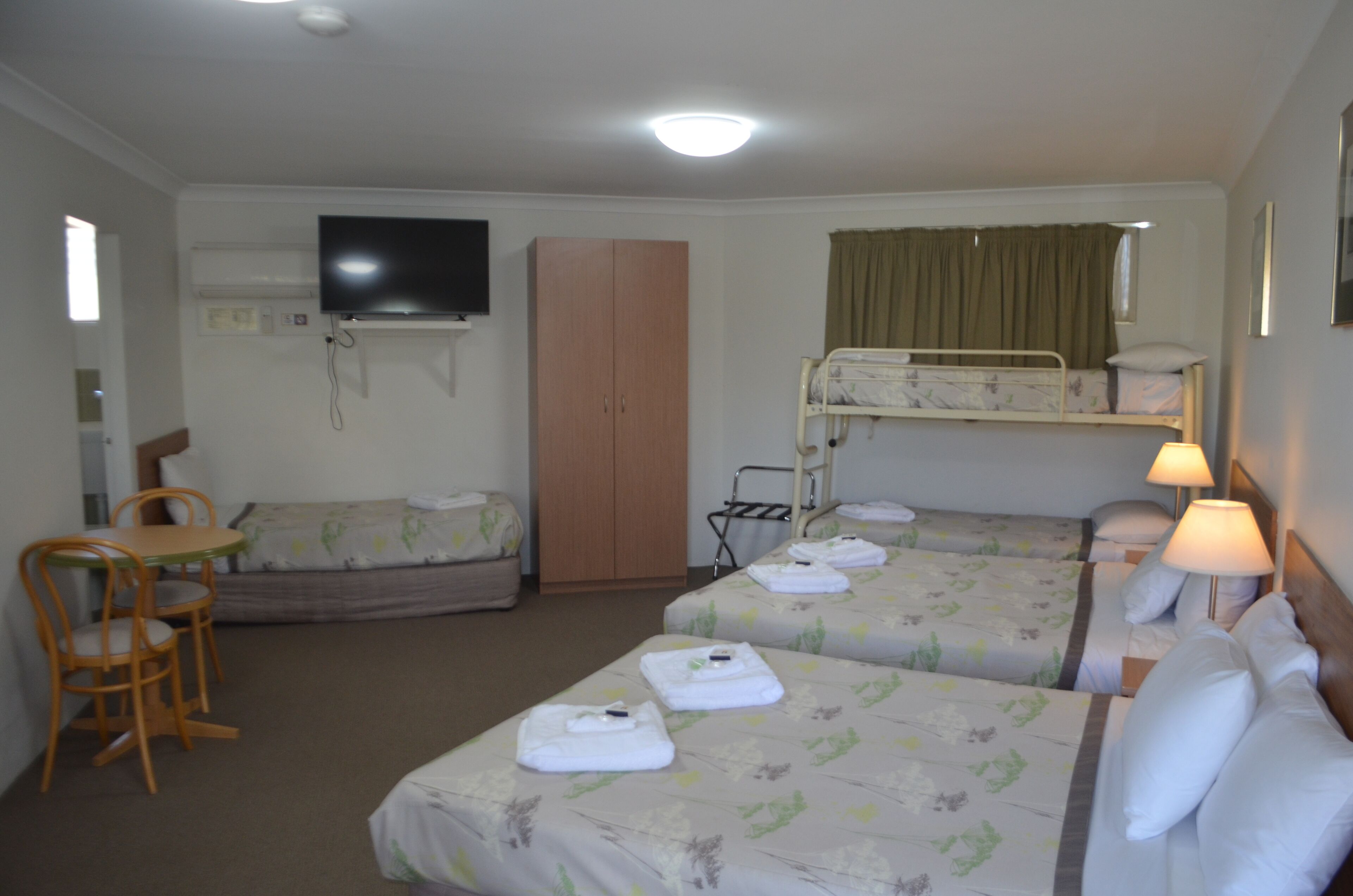 A hotel room with two beds, a TV, a wardrobe, a desk with chairs, and a window with curtains.