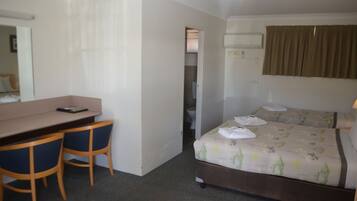 A hotel room with a desk, two chairs, a bed with a floral bedspread, and a bathroom visible through an open door.