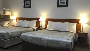A hotel room with two beds, each with a wooden headboard, white bedding, and bedside lamps. There are framed pictures on the wall above each bed.