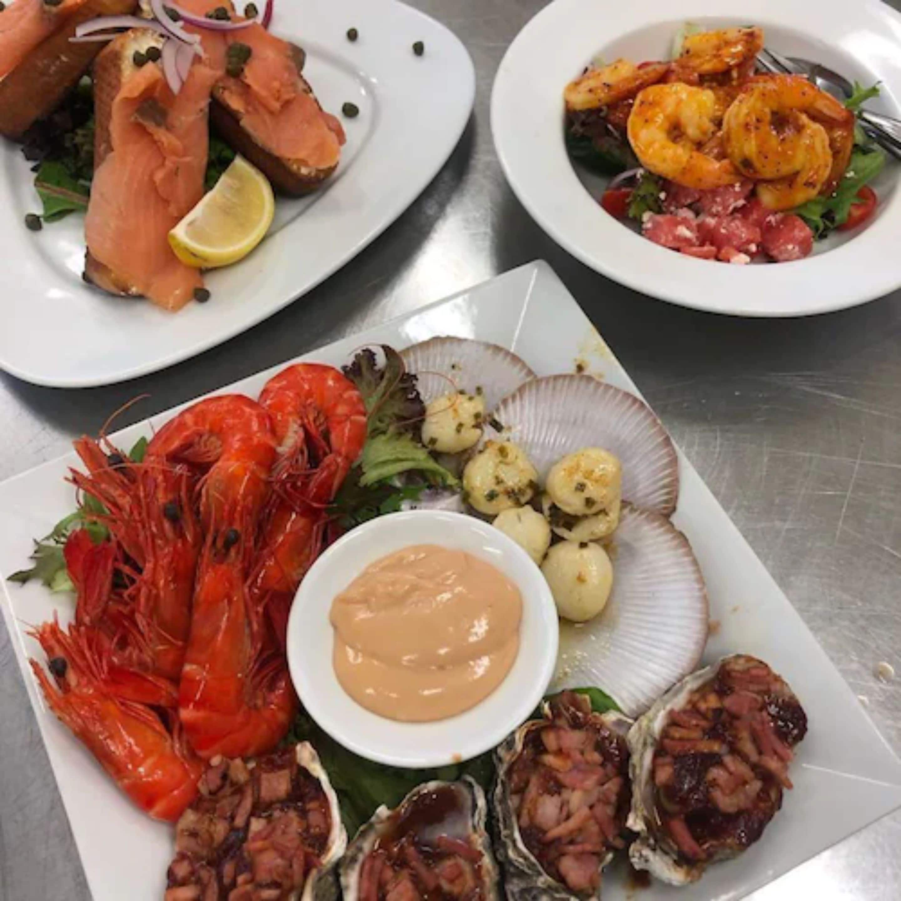 A variety of seafood dishes including shrimp, oysters, and salmon, served on white plates.